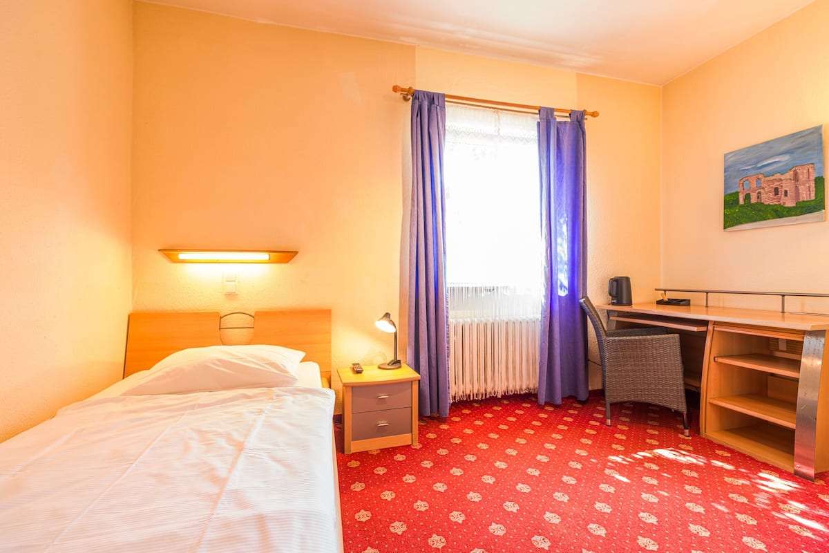 Een hotelkamer met een bed, een bureau, een stoel, een lamp, een nachtkastje en een schilderij aan de muur.