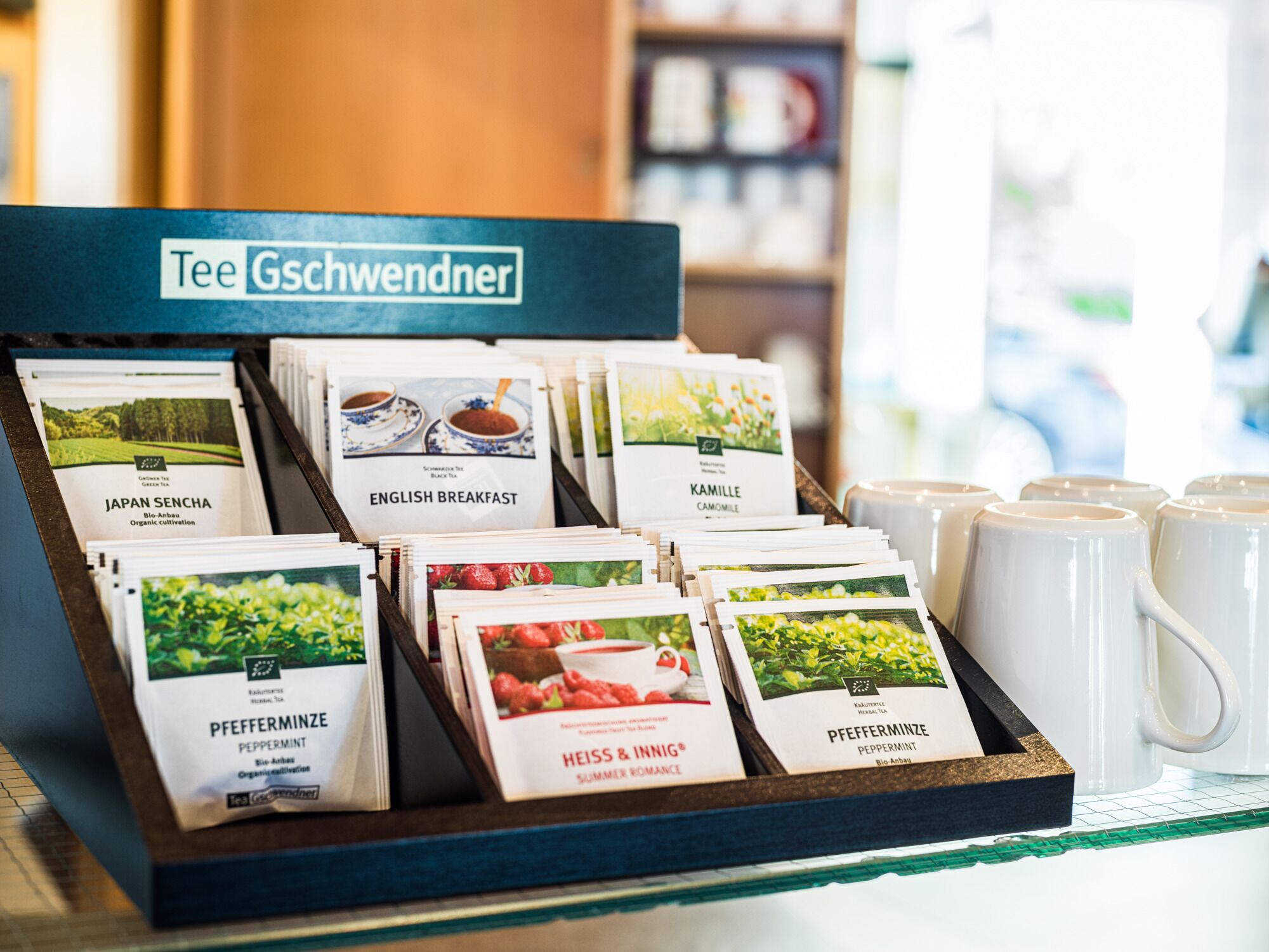 A display of tea bags with labels indicating different flavors and origins, such as Japan Sencha and English Breakfast, at a tea shop.