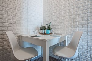 A dining area with a white table and two chairs, a small potted plant, and a glass of wine.