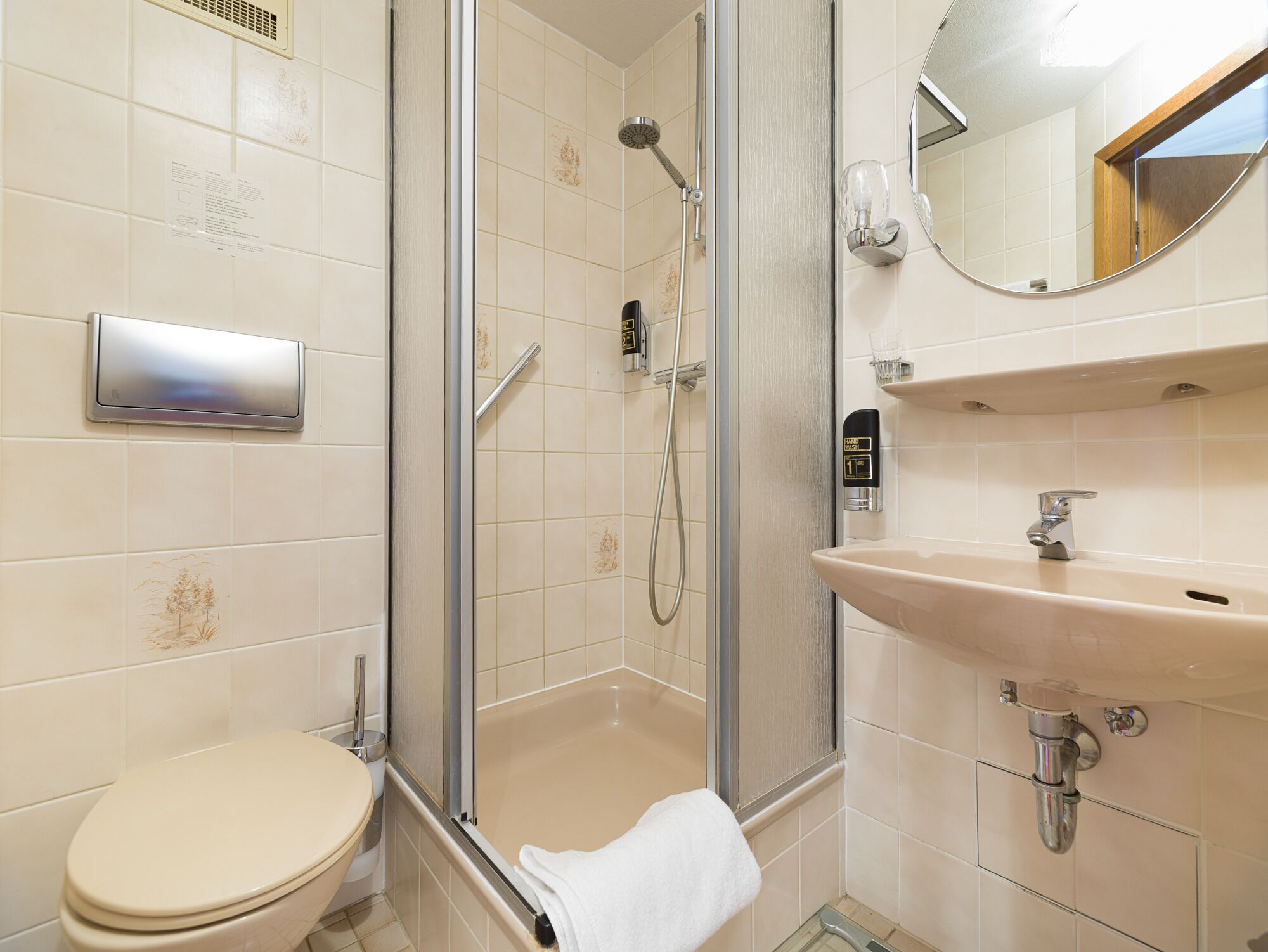 Une salle de bain comprenant des toilettes, une douche fermée par une paroi de verre, un lavabo et un miroir.