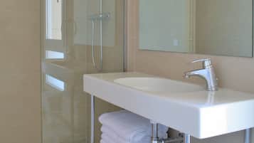 Un baño moderno con ducha envuelta en vidrio, un lavamanos blanco y un espejo encima.