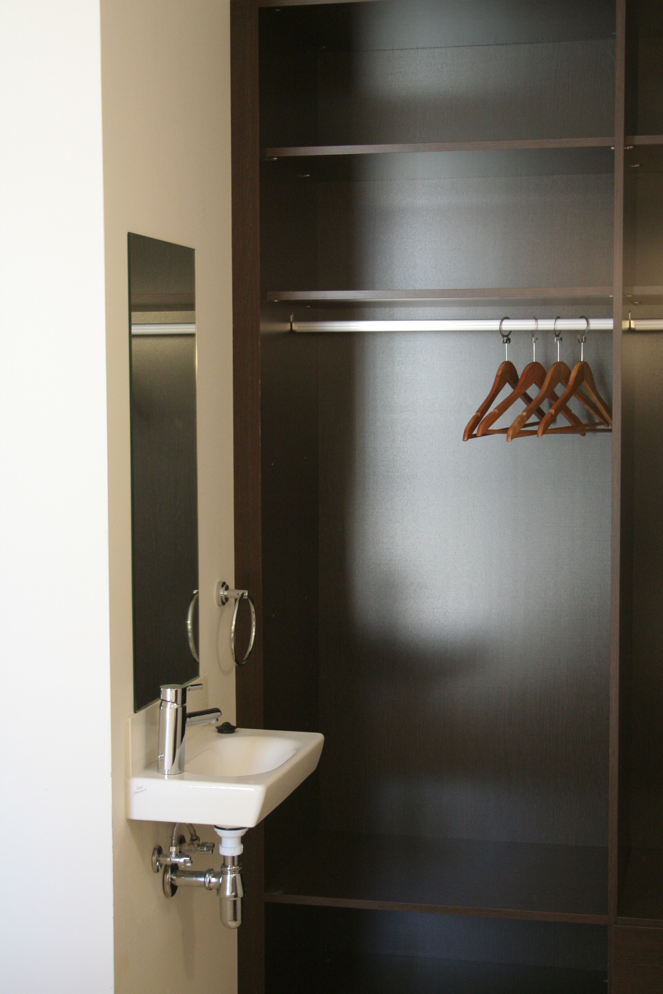 A bathroom with a white sink, a mirror, and wooden hangers on a rack.