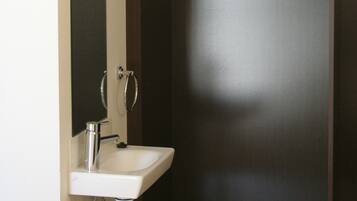 Un baño con un lavamanos blanco, un espejo y perchas de madera en un perchero.