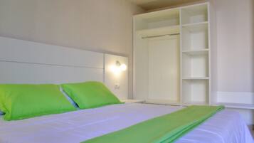 A bed with white bedding and green pillows, a white wardrobe with open doors, and a wall-mounted light fixture.
