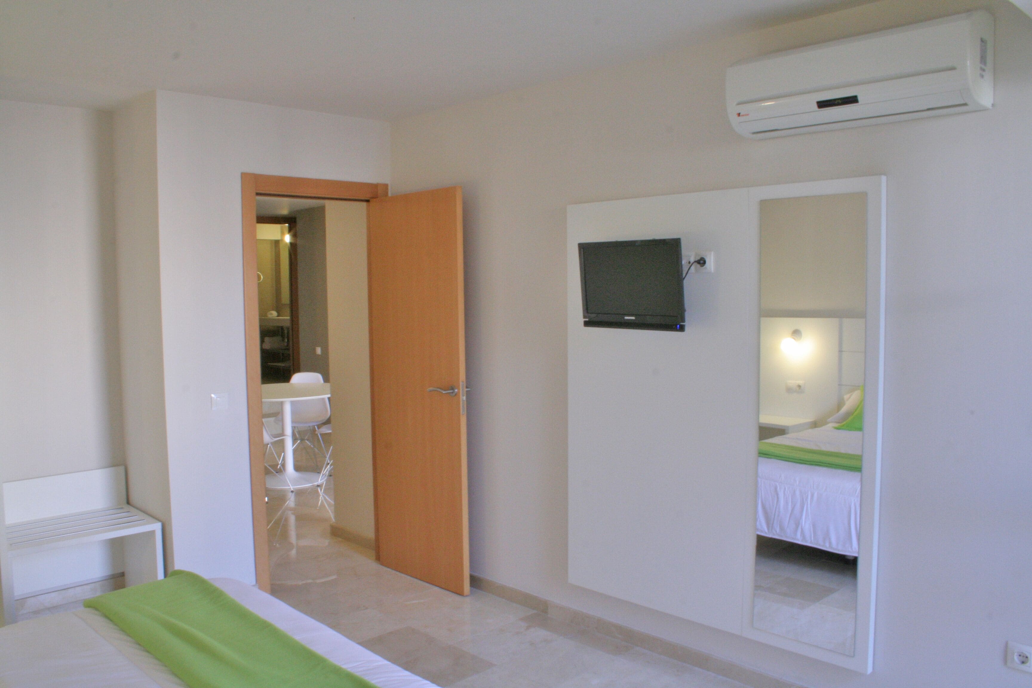 Habitación de hotel con una cama, un televisor montado en la pared, un espejo y un equipo de aire acondicionado.