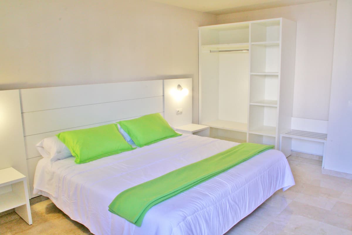A neatly made bed with green pillows and a white headboard in a hotel room.