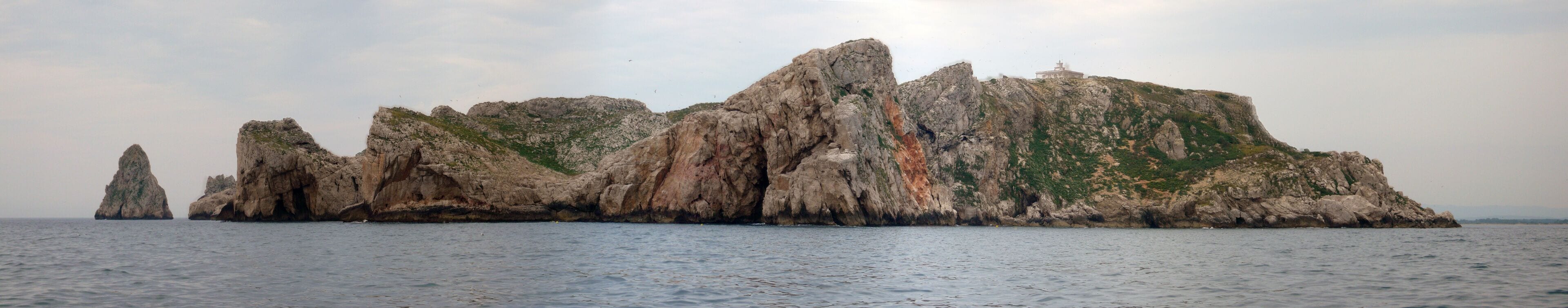 A rocky coastal landscape with a prominent rock formation and a small building on top.
