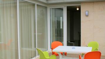 A modern outdoor seating area with a white table and four chairs, one green and three orange, on a wooden deck.