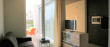 A modern living room with a sofa, a TV, and a kitchen area with a microwave.