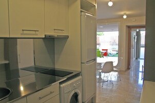 Una cocina moderna con horno empotrado, microondas y lavavajillas. Se observa un comedor con mesa y sillas a través de una puerta abierta.
