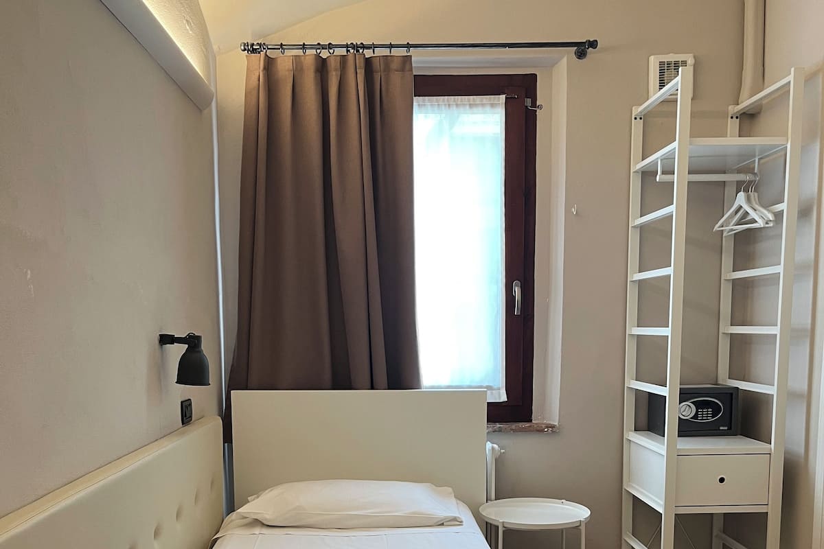 A bedroom with a bed, a bedside table, a wardrobe, and a window with curtains.