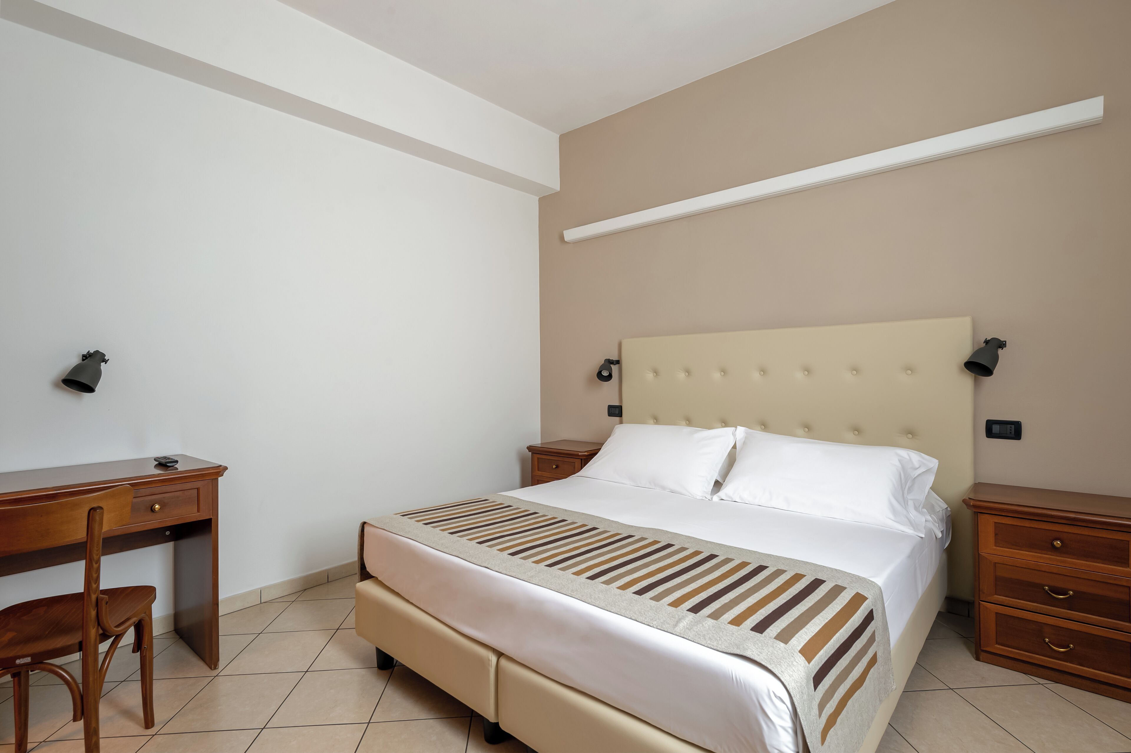 A bedroom with a bed, a desk, a chair, and a nightstand.