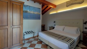 Une chambre à coucher comprenant un lit, une armoire en bois, un sol à carreaux, un tableau représentant un paysage urbain et un mur d’accent en pierre.