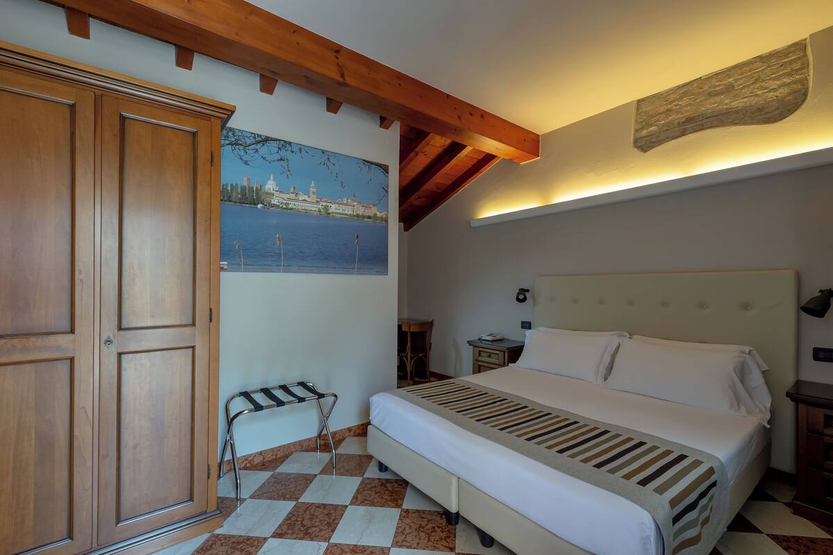 A bedroom with a bed, a wooden wardrobe, a checkered floor, a painting of a cityscape, and a stone accent wall.