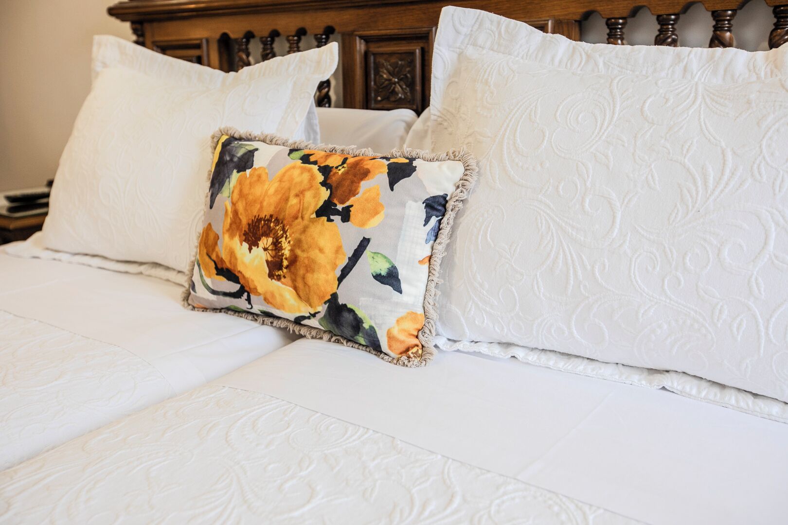 Una cama con sábanas blancas y dos almohadas, una con diseño floral.