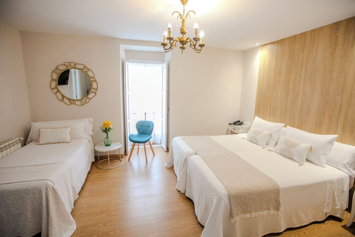 A hotel room with two beds, a small table with a vase of flowers, a blue chair, and a chandelier.