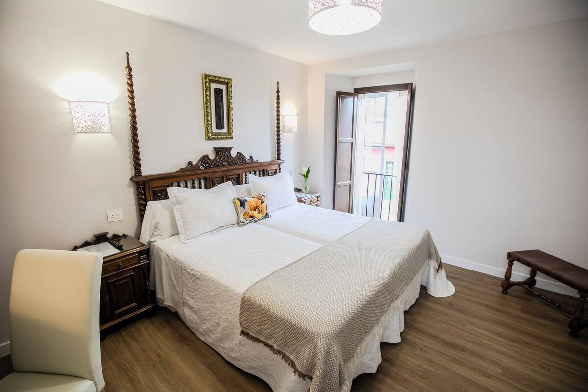 A bedroom with a wooden bed, a nightstand, a chair, a bench, and a door leading to a balcony.