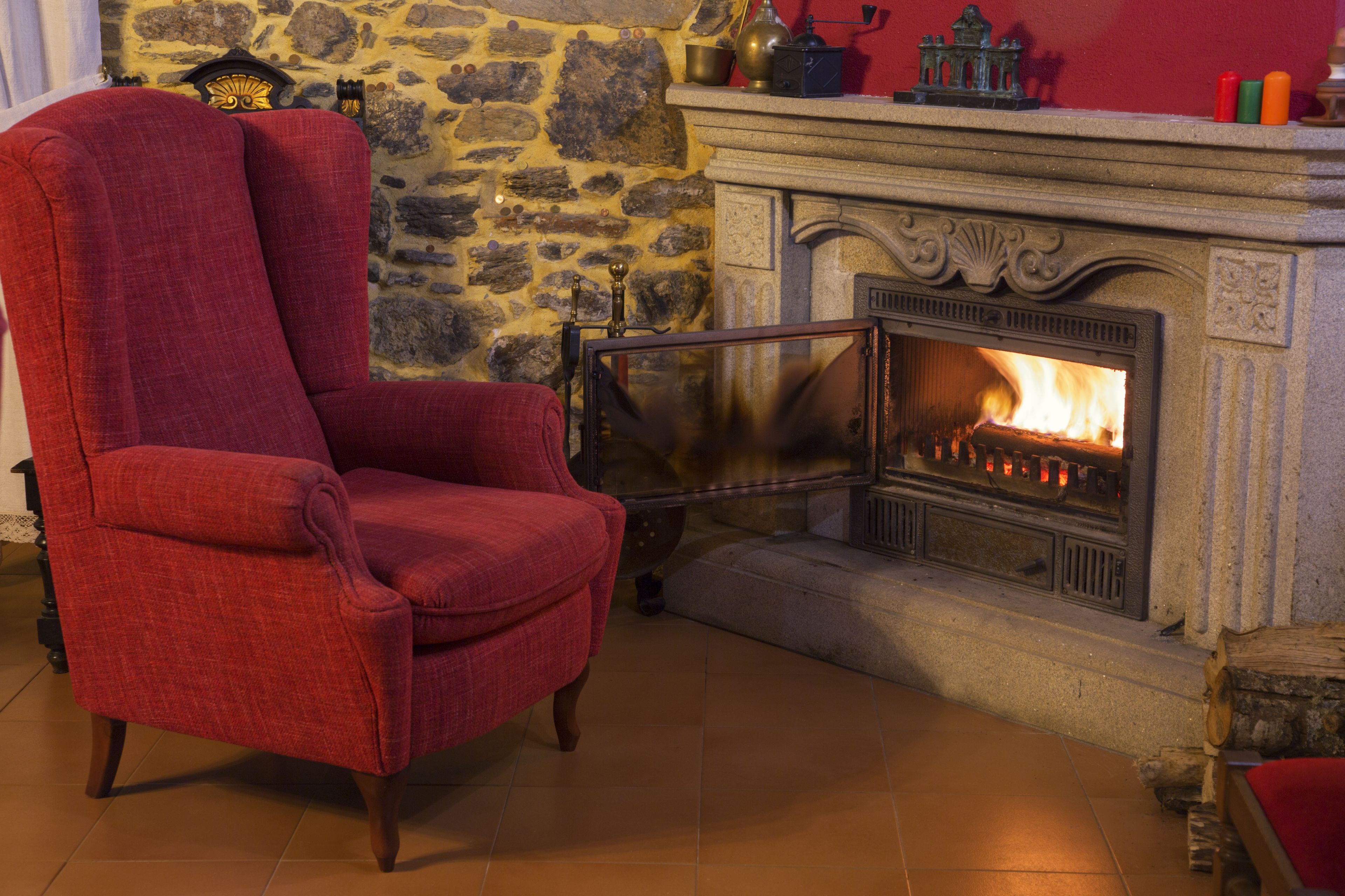 A red armchair in front of a stone wall and a fireplace with a visible fire.