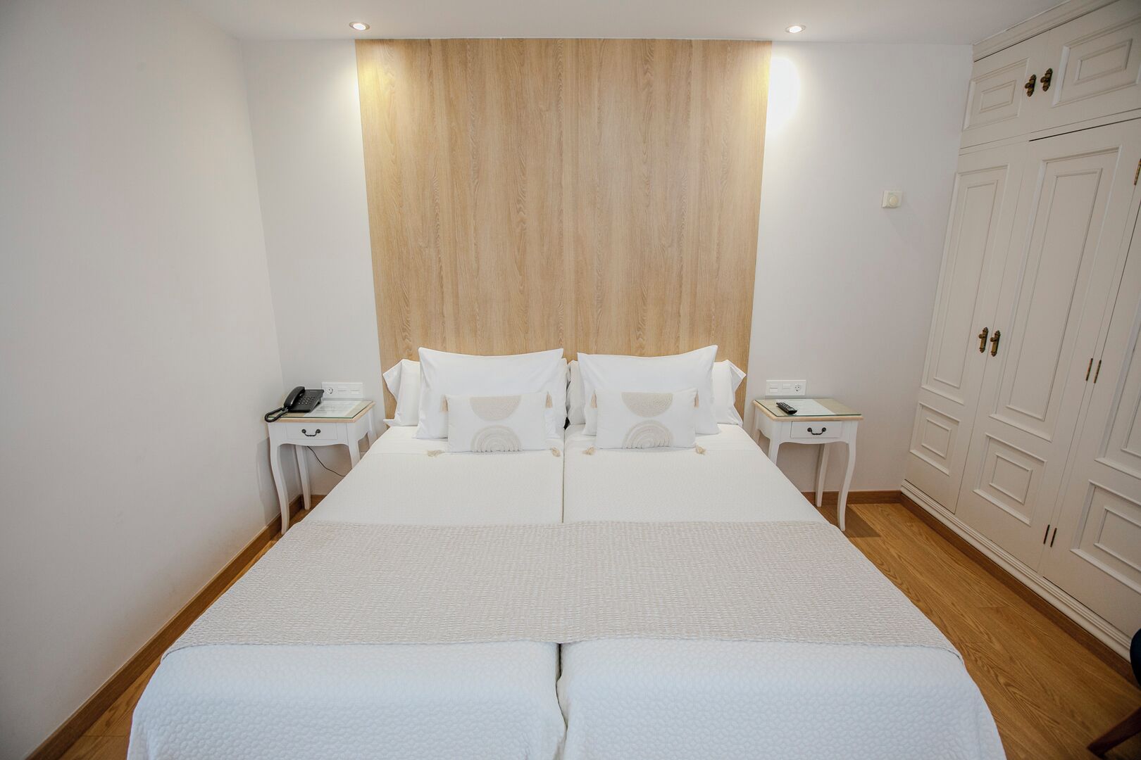 A hotel room with a large bed, two bedside tables, a wooden headboard, and a wardrobe.