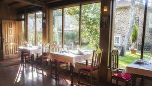 A dining area with tables and chairs, large windows, and a view of the garden.