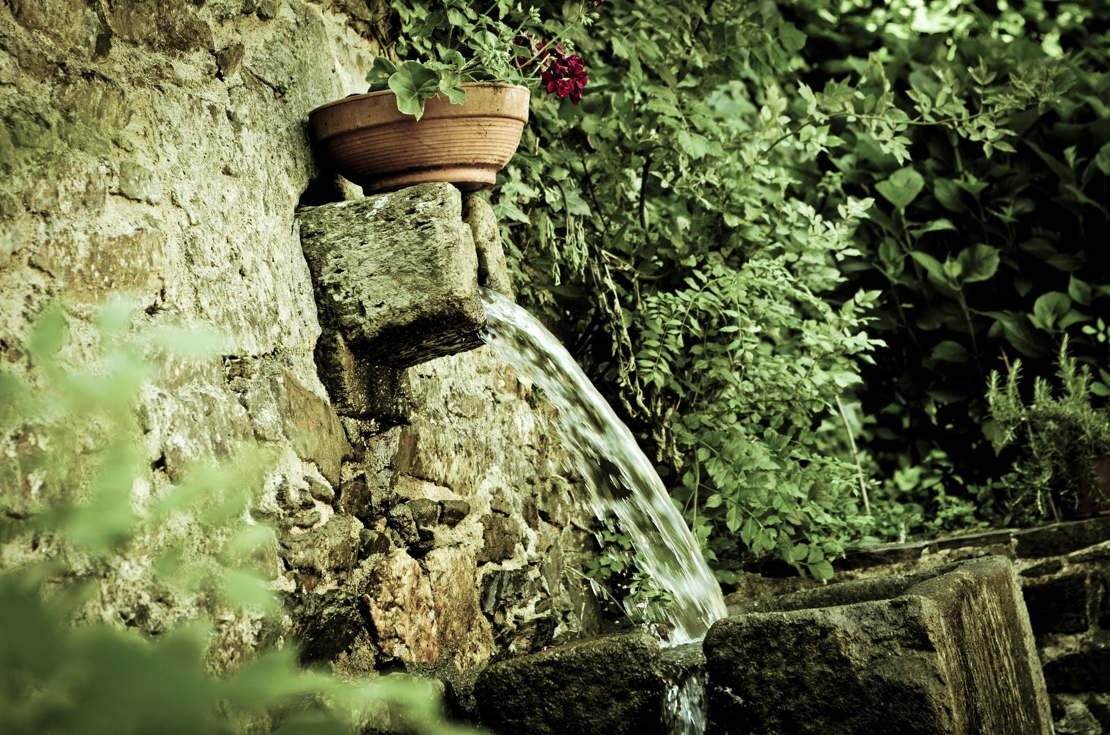 Eine Steinsäule mit integriertem Blumenkasten, der rote Blüten und ein kleines Wasserspiel beherbergt.