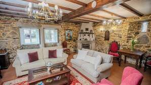 A cozy living room with stone walls, two sofas, a fireplace, and wooden beams.