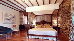 A bedroom with a four-poster bed, wooden flooring, stone walls, and a chandelier.