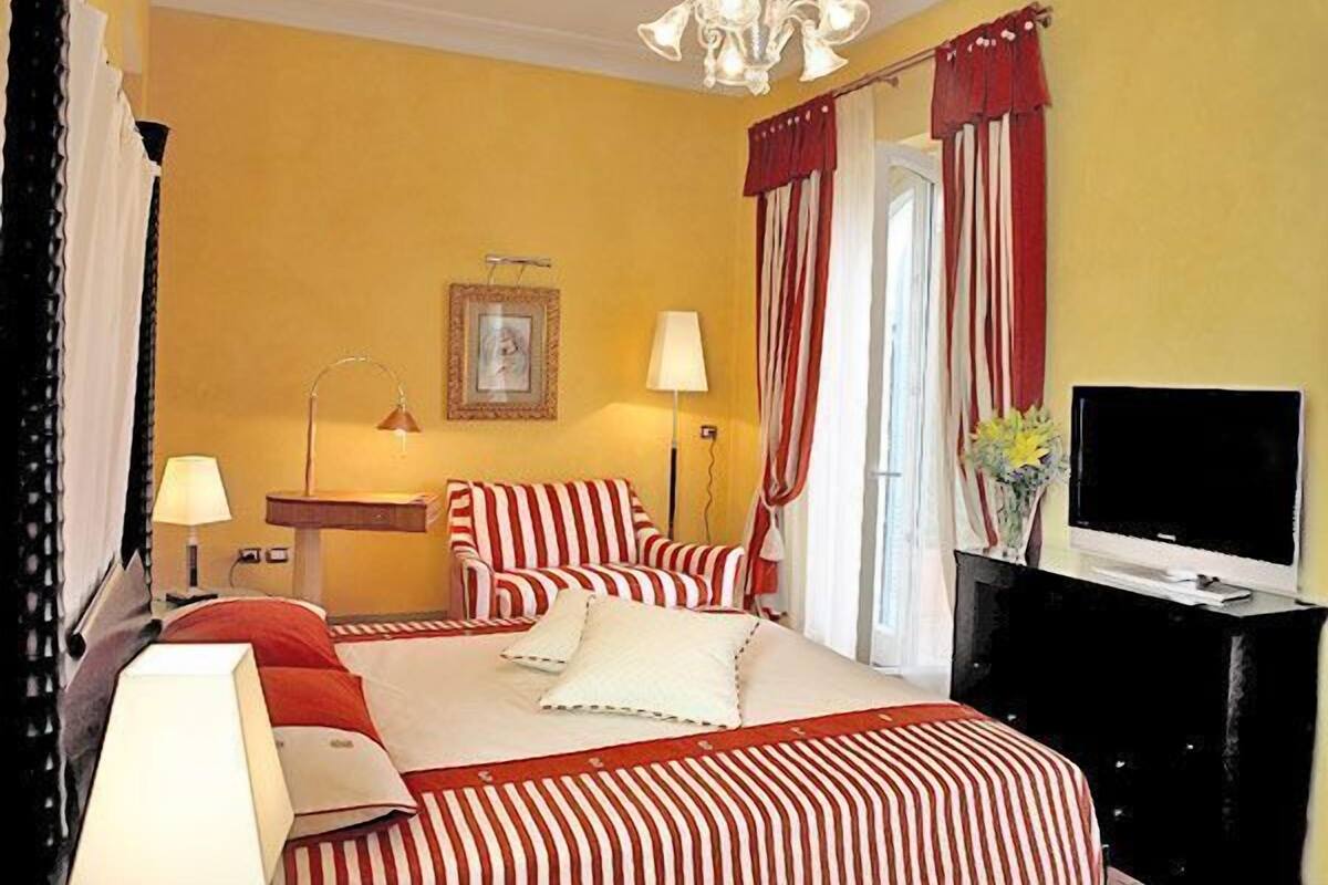 A hotel room with a bed, a TV, a desk with a lamp, and a chair.