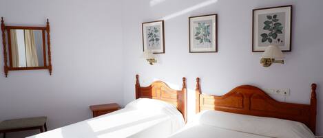 A hotel room with two beds, a wooden headboard, a bedside table, a bench, and wall-mounted artwork.