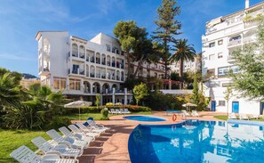 A pool area with lounge chairs and a building with multiple balconies. - Andalucía (Lanjaron)