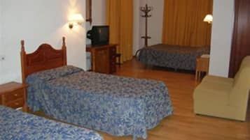 A room with two beds, a wooden floor, a small table with a lamp, and a chair.