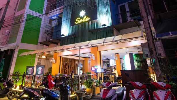 A hotel with a neon sign, multiple floors, and parked scooters in front. - Hotel Sole (Patong)