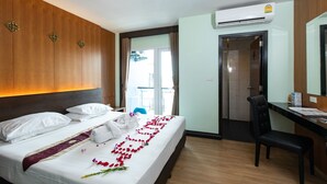 A hotel room with a bed, a desk, and a chair. There is an air conditioning unit on the wall and a window with curtains. - Hotel Sole (Patong)