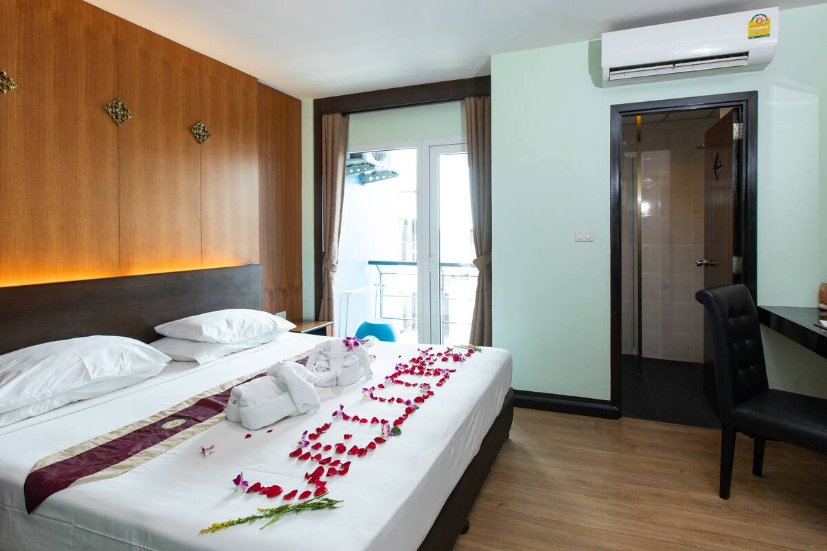 A hotel room with a bed, a desk, and a chair. There is an air conditioning unit on the wall and a window with curtains.