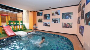 An indoor swimming pool with a slide and play area, surrounded by walls decorated with movie posters. - Hotel Sole (Patong)