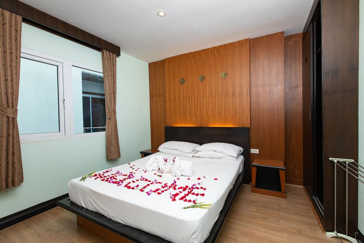 A neatly made bed with white linens and a floral arrangement, a wooden headboard, and a bedside table with a lamp.