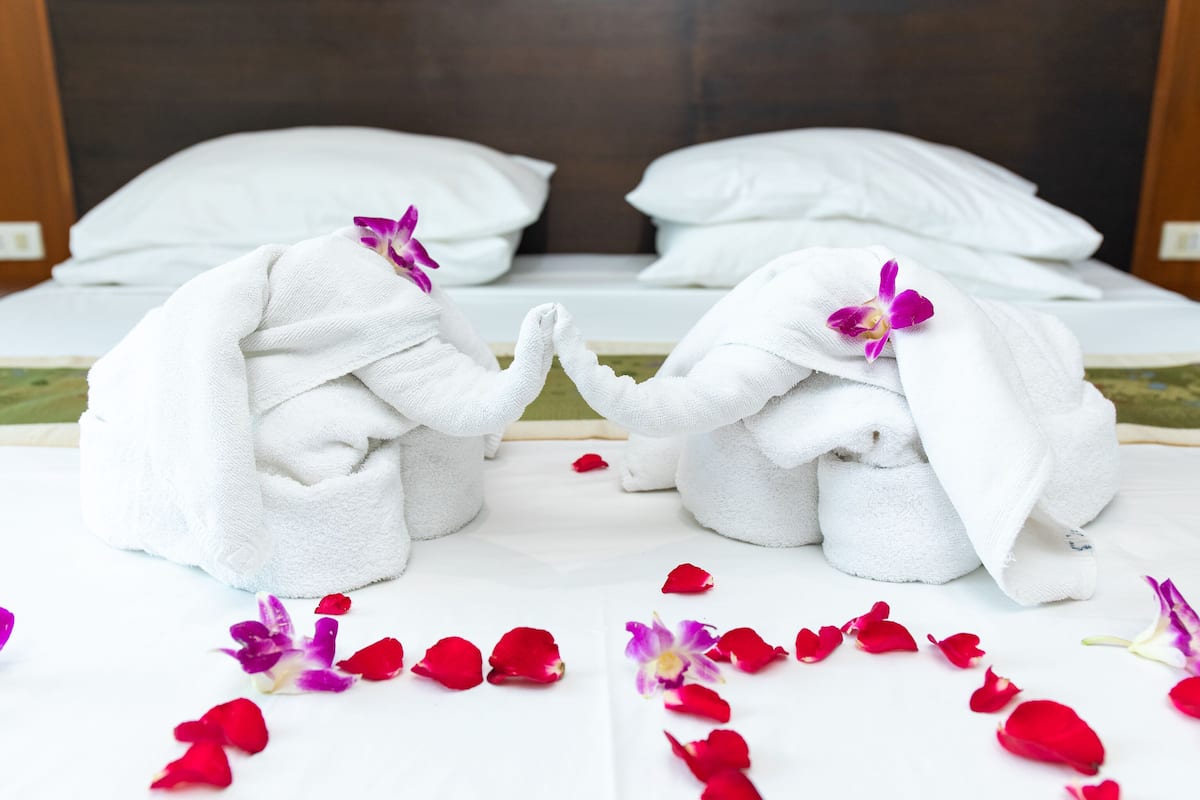 A neatly made bed with white linens and a purple orchid.