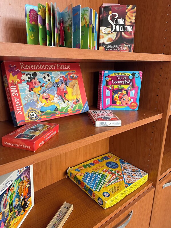 Una estantería con varios juegos de mesa y rompecabezas, incluyendo 'Ravensburger Puzzle' y 'Mercante in fiera'.