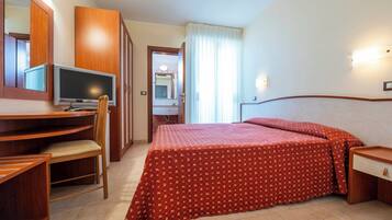 A hotel room with a bed, a desk, a chair, a television, and a mirror.