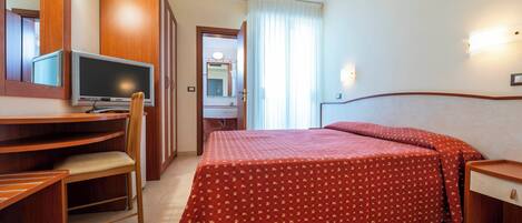Una habitación de hotel con cama, escritorio, silla, televisor y espejo.