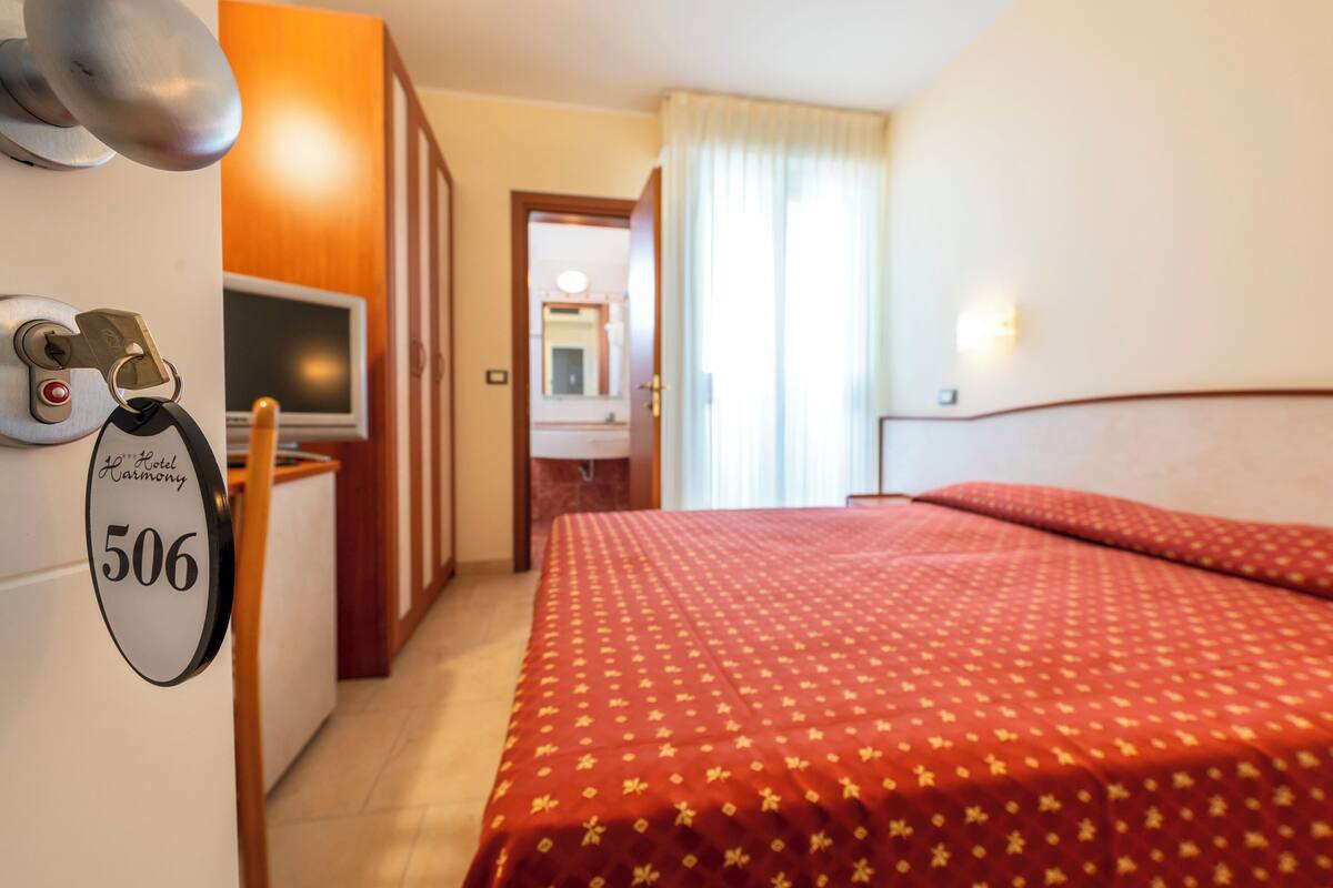 A hotel room with a bed, a desk with a television, a minibar, and a door with a keycard lock.