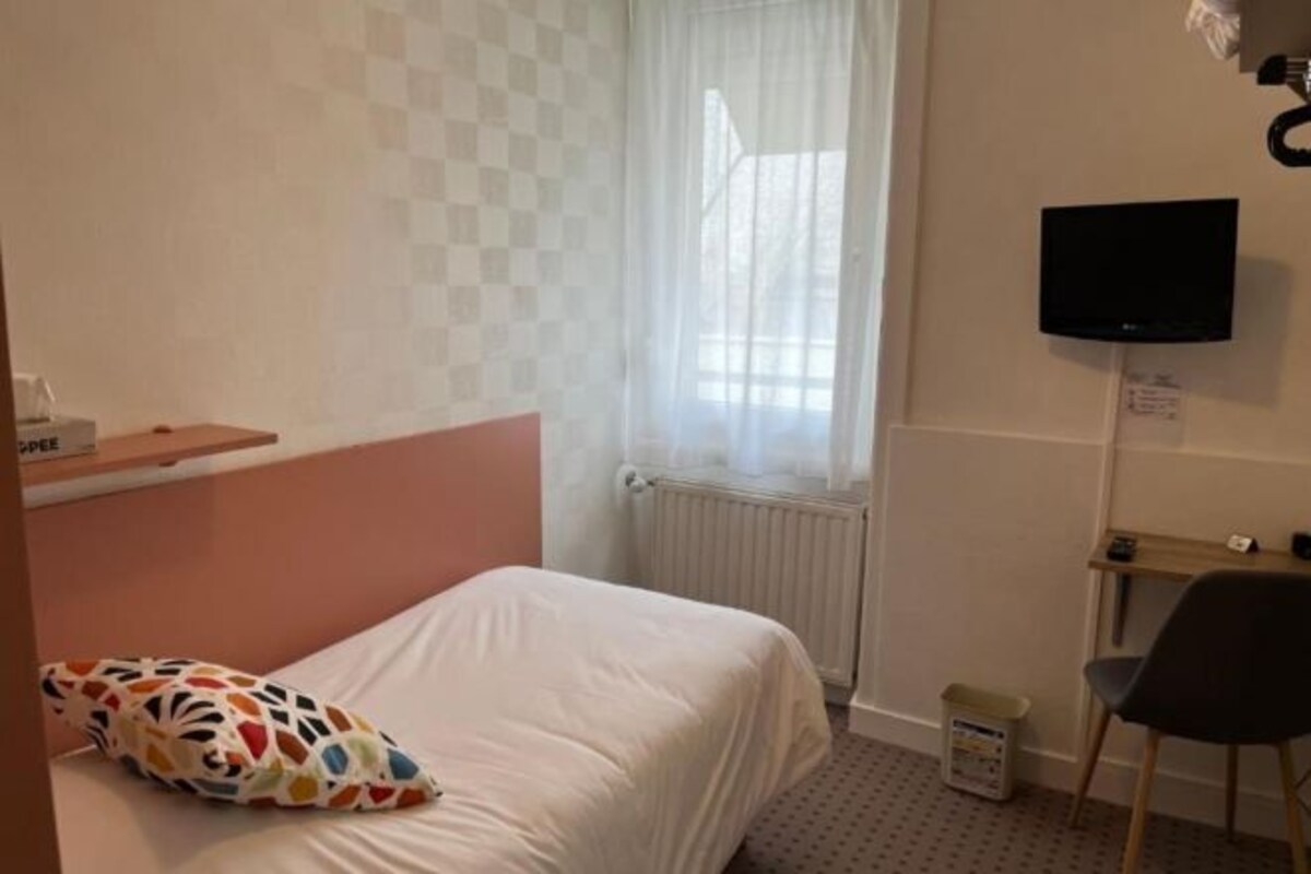 A hotel room with a bed, a TV mounted on the wall, a small desk, and a chair.