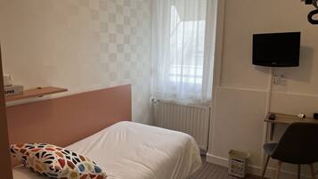 A hotel room with a bed, a desk, a chair, a TV, a radiator, and a window with curtains.