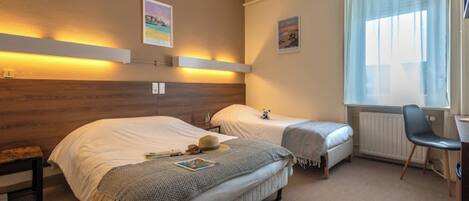 Quarto de hotel com duas camas, uma escrivaninha e uma cadeira.