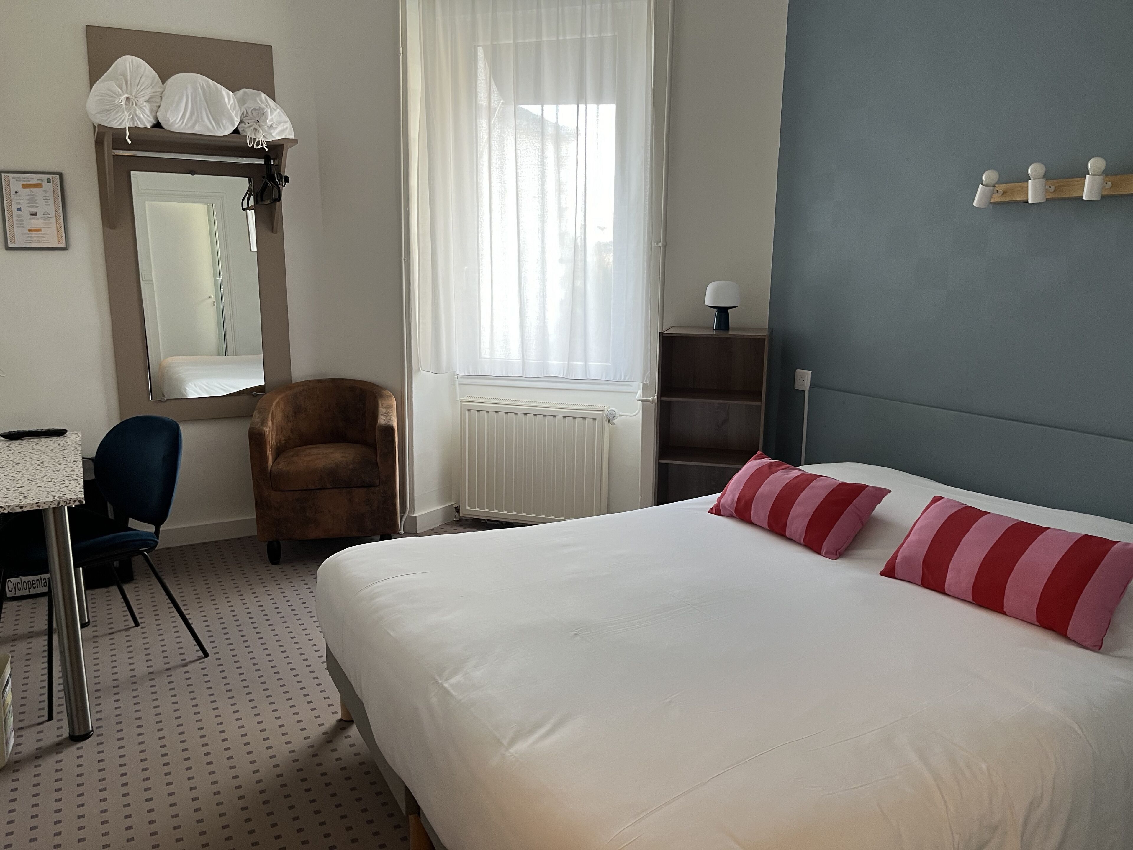 Habitación de hotel con cama, una silla, escritorio, espejo y ventana con cortinas.