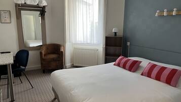 Una camera d'albergo con un letto, una sedia, una scrivania, uno specchio e una finestra con tende.