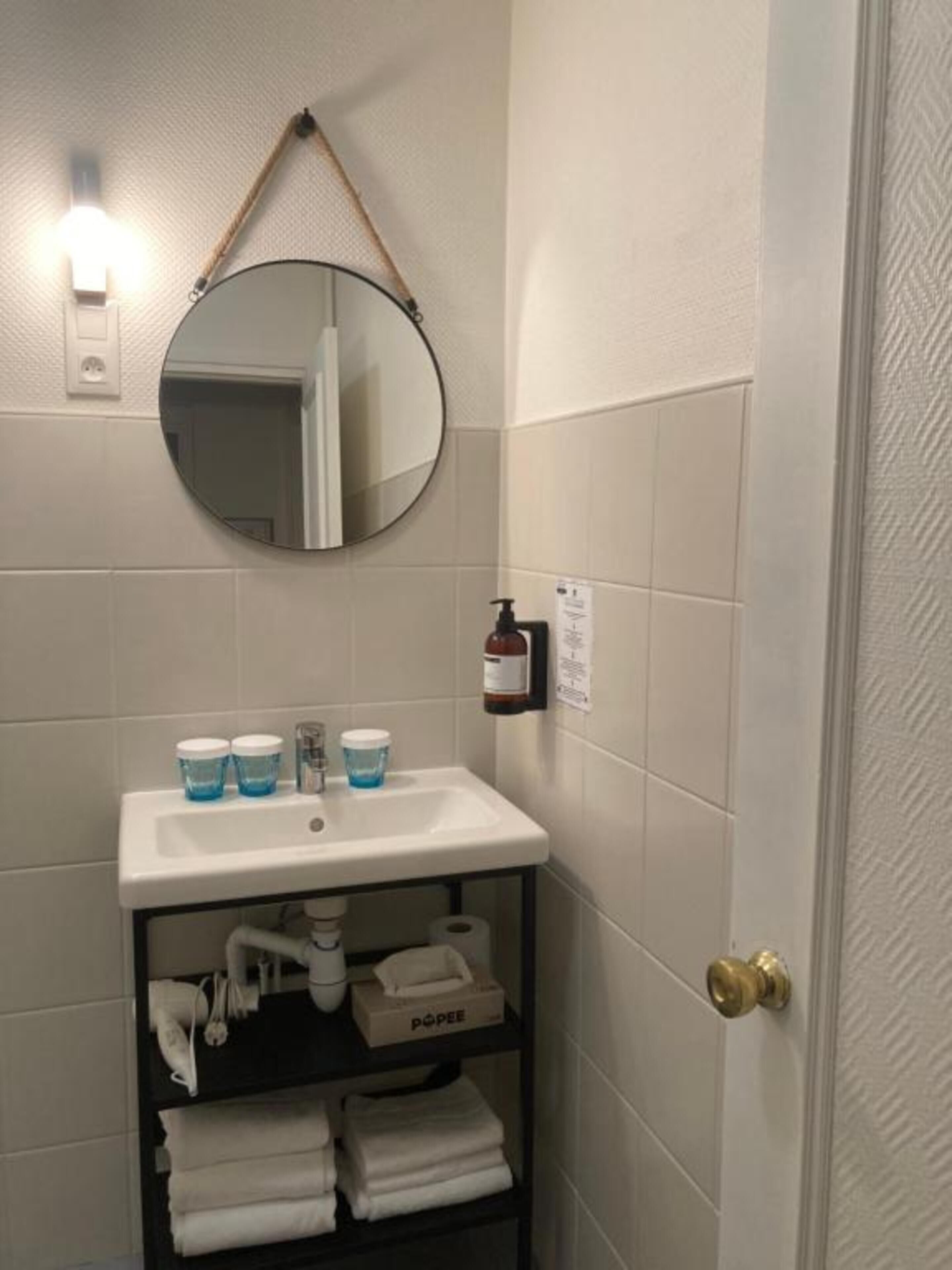 Un baño con lavamanos blanco, un espejo redondo y un perchero para toallas.