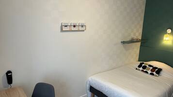 Une chambre d’hôtel équipée d’un lit, d’un bureau, d’une chaise, d’une étagère fixée au mur et d’une prise électrique murale.