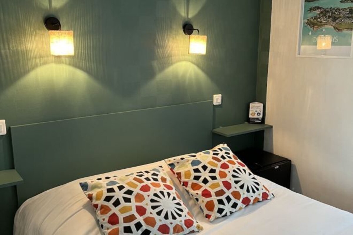 A hotel room with a bed, two wall-mounted nightstands, and two wall sconces.