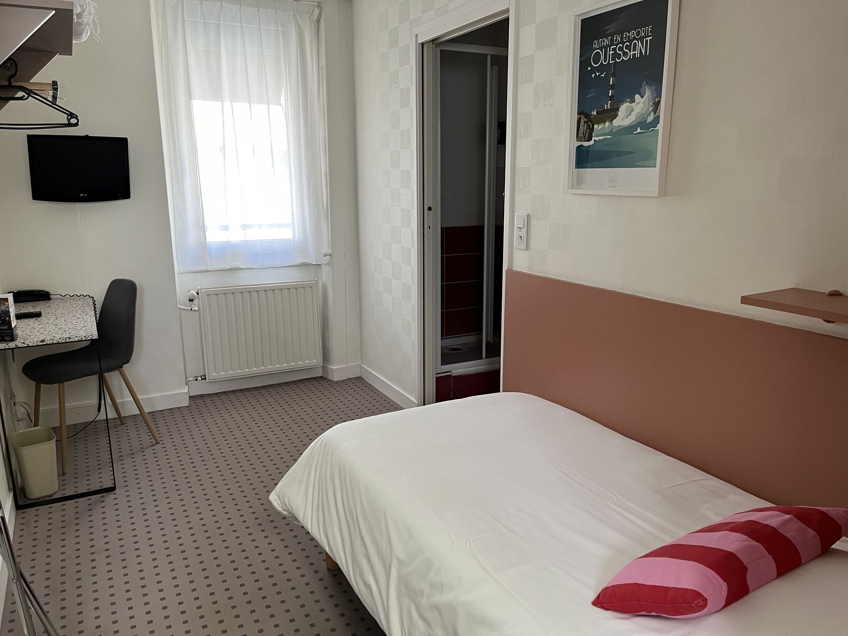 A bedroom with a bed, a desk, a chair, a radiator, a window with curtains, and a poster on the wall.